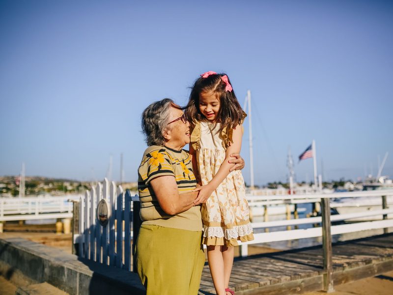A grandmother and her granddaughter embrace on a sunny harbor dock.